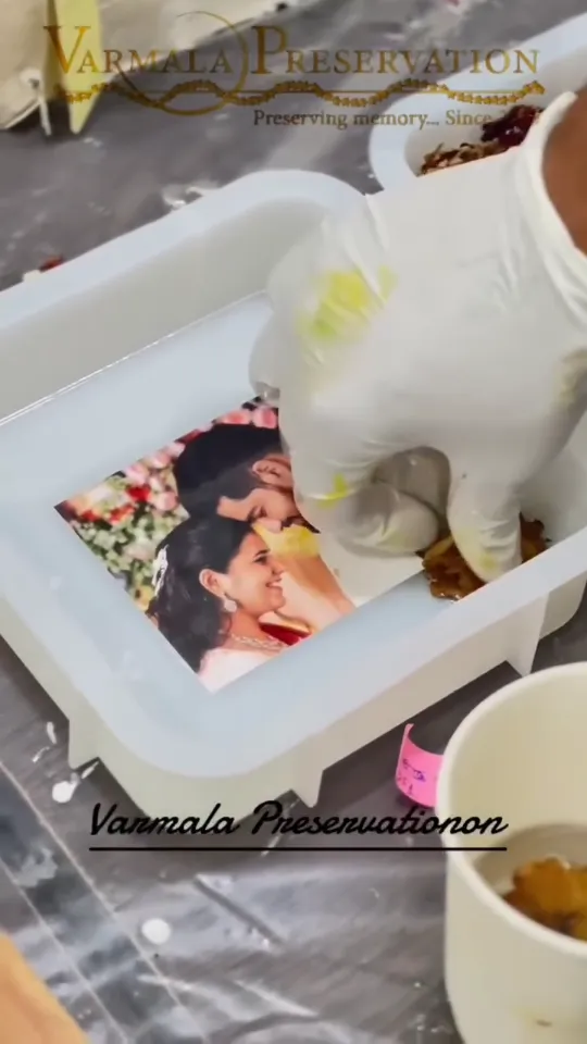 Resin being poured over a couple photo and varmala flowers in a round mould
